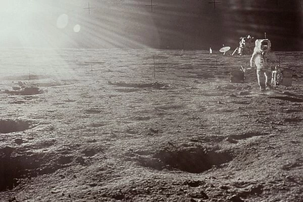 APOLLO 12: ASTRONAUT. Astronaut Alan Bean carrying components of the ALSEP (Apollo Lunar Surface Experiments Package) during the Apollo 12 mission, 19 November 1969, with lunar module in background, against the suns glare